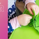 Des mains d'enfant en train de coudre un tissu vert