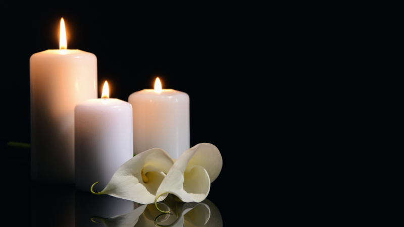 Trois bougies blanches allumées avec une fleur blanche sur un fond noir
