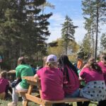 Les élèves participants assis en groupe avec des t-shirts bleus, roses, verts et oranges à l'atelier de Christian Pilon en plein air
