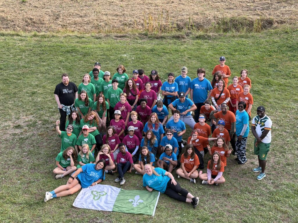 Élèves de 7e et 8e en t-shirts de couleur verte, bleue, rose et orange en photo de groupe lors du camp leadership 2025